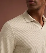 Polo de manga larga color beige claro, confeccionado en tejido texturizado (posiblemente acanalado o waffle). Presenta un cuello polo con escote profundo en V sin botones.