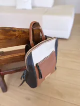 Mochila de cuero tricolor en tonos marrón tostado, negro y blanco, con bolsillo frontal con cierre, tiradores de cuero y detalle de etiqueta con logo grabado.