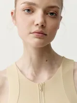 Top deportivo color beige, de cuello redondo con cierre frontal parcial y diseño ajustado.