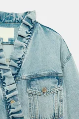Cazadora de denim color celeste con cuello alto y volantes en el borde frontal. Cuenta con cierre cruzado con botones metálicos y bolsillos en el pecho con solapa.