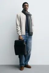 Mochila negra de poliuretano, con solapa y cierre de hebilla. Tiene un compartimento principal con espacio para dispositivos electrónicos de hasta 13 pulgadas y un bolsillo con cierre. En la parte frontal tiene un bolsillo con cierre y bolsillos planos en la parte frontal y posterior. Tiene asa de mano y dos asas de hombro ajustables y acolchadas.