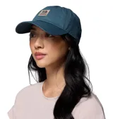 Gorro unisex de algodón color azul verdoso, con visera curva y cierre de velcro ajustable en la parte trasera. Presenta un parche frontal bordado con el logo de Columbia Sportswear y un oso.