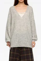 Jersey de punto largo con corte oversize, escote en pico pronunciado y mangas largas con volumen. Incluye un top interior de tirantes en satén con detalles de encaje en el escote.