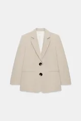 Blazer sastre de corte recto, color beige, con cuello solapa, hombreras marcadas y cierre frontal de dos botones oscuros. Cuenta con bolsillos con solapa en el frente y un bolsillo ojal en el pecho.
