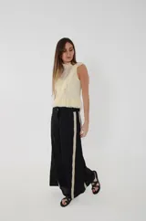 Pantalón de lino negro con franjas laterales en tono beige y pespuntes en hilo color óxido. Presenta corte amplio de piernas anchas, cintura media y un bolsillo trasero con bordado de una rosa en hilo contrastante.