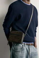 Bandolera combinada de diseño rectangular, confeccionada en gamuza marrón con detalles de cuero liso y correa larga ajustable. Cuenta con cierre principal de cremallera y bolsillo plano en el interior.