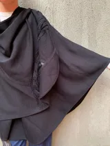 Capa negra de tejido de punto en lana con apliques de cuero y cuello drapeado.