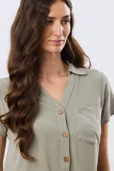 Camisa lisa de lino color beige, de manga corta, con cuello camisero, bolsillo ojal en el pecho y cierre frontal con botones.