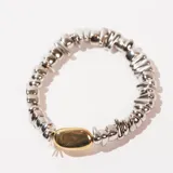 Pulsera elástica con cuentas irregulares plateadas y una cuenta central ovalada dorada.