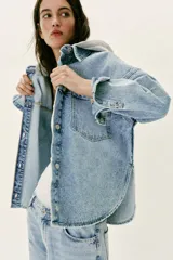Cazadora de denim oversize con capucha gris desmontable, cuello camisero, cierre frontal con botones metálicos y bolsillos delanteros de plastrón.