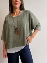 Conjunto de dos piezas compuesto por una remera básica blanca de algodón y un buzo liviano de textura plisada en color verde oliva. El buzo presenta mangas murciélago, corte holgado y detalles de hilo plateado en los bordes. Incluye un collar decorativo con dije circular.