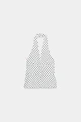 Top halter entallado de color blanco con estampado de lunares negros, escote en V pronunciado, espalda descubierta y cierre frontal con ganchos metálicos.