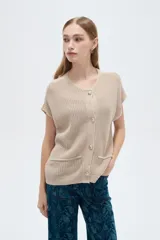 Chaleco de manga corta tejido en acrílico, color beige, con escote en V, cierre frontal de botones y bolsillos delanteros aplicados.