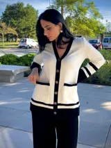 Cardigan de punto en color blanco con detalles en negro en los bordes, cuello en V, cierre frontal con botones dorados y bolsillos delanteros.
