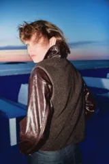 Chaleco de tejido sherpa (borreguito) color marrón oscuro, con cuello redondo y cierre frontal de botones. Presenta ribetes de cinta a tono y bolsillos redondos en la parte delantera.