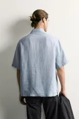 Camisa regular fit confeccionada en tejido de lino, color blanco, con cuello solapa, manga corta y cierre frontal de botonadura.