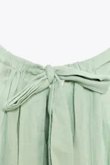 Top de gasa color menta con cuello halter y lazada posterior. Presenta detalles de bordados calados a tono y un bajo con terminación en volante.