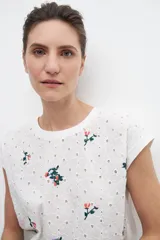 Blusa blanca con bordados florales y broderie en el frente, de manga corta y corte recto.