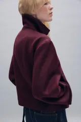 Abrigo corto de paño con mezcla de lana, color bordó. Presenta cuello subido, cierre frontal cruzado con botones, mangas largas con trabillas decorativas y bolsillos laterales de vivo.