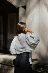 Camisa de algodón con diseño a rayas verticales en tonos blanco y gris. Presenta un corte oversize con mangas abullonadas y un nudo frontal que permite ajustar la prenda a la cintura.