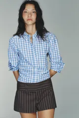 Camisa de manga larga con cuello solapa y cierre frontal de botones. Tejido de popelín 100% algodón con estampado a cuadros azules y blancos. Bajo con corte evasé.