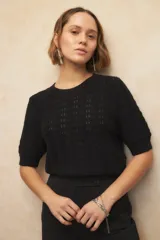 Top de tejido tramado negro, de manga corta y cuello redondo a la base. Presenta elástico en el ruedo y en los puños de las mangas.