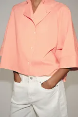 Camisa ZARA Woman Collection confeccionada en hilatura con viscosa, con diseño de rayas finas y color salmón. Presenta cuello perkins, mangas por debajo del codo, bajo asimétrico y cierre frontal cruzado con botones.