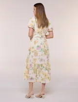 Vestido maxi de gasa color beige con estampado floral en tonos amarillos y rosados, escote en V cruzado, mangas cortas abullonadas y cintura elastizada con nido de abeja.