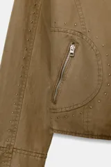 Chaqueta de cuello subido con cierre frontal de cremallera, bolsillos delanteros con cremallera y detalle de tachas metálicas decorativas en mangas y cuerpo. Cuenta con forro interior.