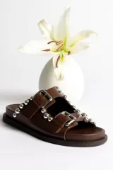 Sandalias marrones de cuero con doble tira, hebillas plateadas y apliques de tachas redondas plateadas.