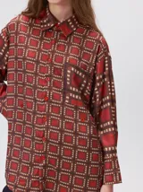 Camisa de seda con cuello camisero, manga larga y bolsillo frontal. Presenta un diseño estampado geométrico de cuadrados en tonos marrones y azul oscuro.
