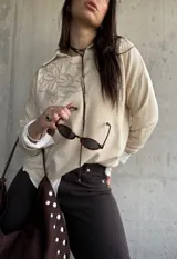 Sweater de punto color beige con bordado floral en el pecho, mangas largas y cuello redondo.