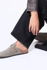 Zueco de gamuza color negro con diseño de punta redonda, ajuste mediante tira con hebilla metálica y suela de corcho.