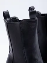 Bota tipo chelsea de caña alta confeccionada en cuero sintético, con paneles elásticos laterales, plataforma dentada y taco cuadrado.