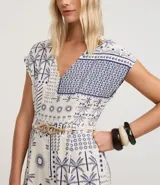 Enterito corto sin mangas de viscolino, con escote en V y estampado tipo patchwork en tonos blanco y azul marino, con motivos tropicales como palmeras y patrones geométricos. Incluye trabillas en la cintura y cinturón de cuerda trenzada.