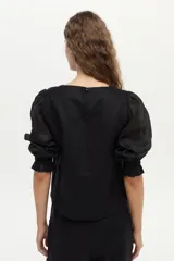 Blusa de lino blanca con escote redondo y mangas cortas abullonadas con detalles de volados en los puños.