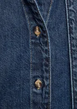 Camisa de jean con cuello camisero y lazo integrado en el frente. Presenta cierre frontal con botones, mangas largas con puños rectos y un corte recto clásico.