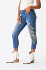 Jeans de corte ajustado y tiro medio en color azul, con detalles de bordados florales coloridos en una de las piernas.
