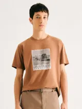 Camiseta blanca de algodón con cuello redondo y mangas cortas. Estampa rectangular con borde negro que contiene la frase "NATURAL ATMOSPHERE" en letras mayúsculas y una imagen de montañas y mar.