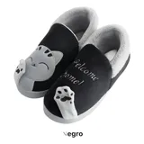 Pantuflas cerradas de piel sintética en color negro, con interior forrado en peluche gris. Presentan un diseño de gatito con apliques bordados en la parte frontal y la frase 'Welcome home!'. Cuentan con suela de goma antideslizante.