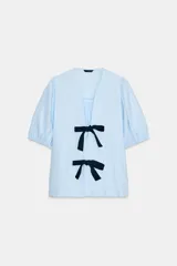 Camisa celeste de lino con escote en pico y manga corta abullonada. Cierre frontal con dos lazos negros a contraste.