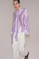 Camisa de ZARA Woman Collection confeccionada en hilatura con mezcla de lyocell, de color blanco marfil. Presenta cuello redondo, escote en V con lazadas en el mismo tejido, manga larga con puño y bajo recto.