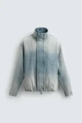Cazadora relaxed fit de denim de algodón con efecto lavado degradado de azul a blanco. Tiene cuello subido, manga larga, bolsillos laterales en la costura de la cadera y acabados con elástico interior. El cierre frontal es con cremallera oculta por una solapa con botones a presión.