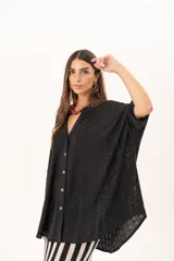 Camisa negra de corte oversize con diseño de encaje calado, escote en V, cierre frontal con botones y mangas tres cuartos. Presenta un diseño asimétrico con la parte posterior ligeramente más larga.