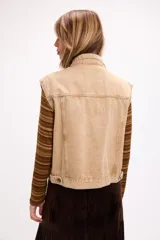 Chaleco de denim con lavado desgastado, corte relajado, cuello camisero, cierre frontal con botones metálicos y bolsillos con solapa en el pecho.