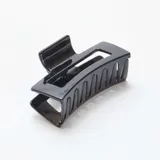 Pack de dos pinzas para el pelo, una con forma de espiral y otra rectangular con diseño calado, ambas de color negro.