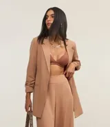 Blazer de sastrería alargado color beige, con cuello con solapa, manga larga con pliegas en el puño y abertura frontal total.