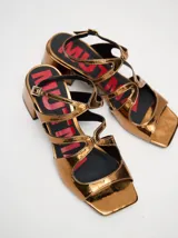 Sandalias de cuero con acabado de charol metalizado en color dorado, con tiras cruzadas en el empeine, taco cuadrado de 4,5 cm y correa ajustable en el tobillo.