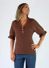 Top de tejido de punto color terracota, con escote en V, cuello camisero y cartera frontal con botones. Presenta mangas cortas con textura calada y puños con volados.
