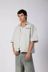 Camisa de manga corta de poplín a cuadros, con calce boxy y largo a la cintura, corte recto, bolsillo superior con estampa y canesú cortado en diagonal.